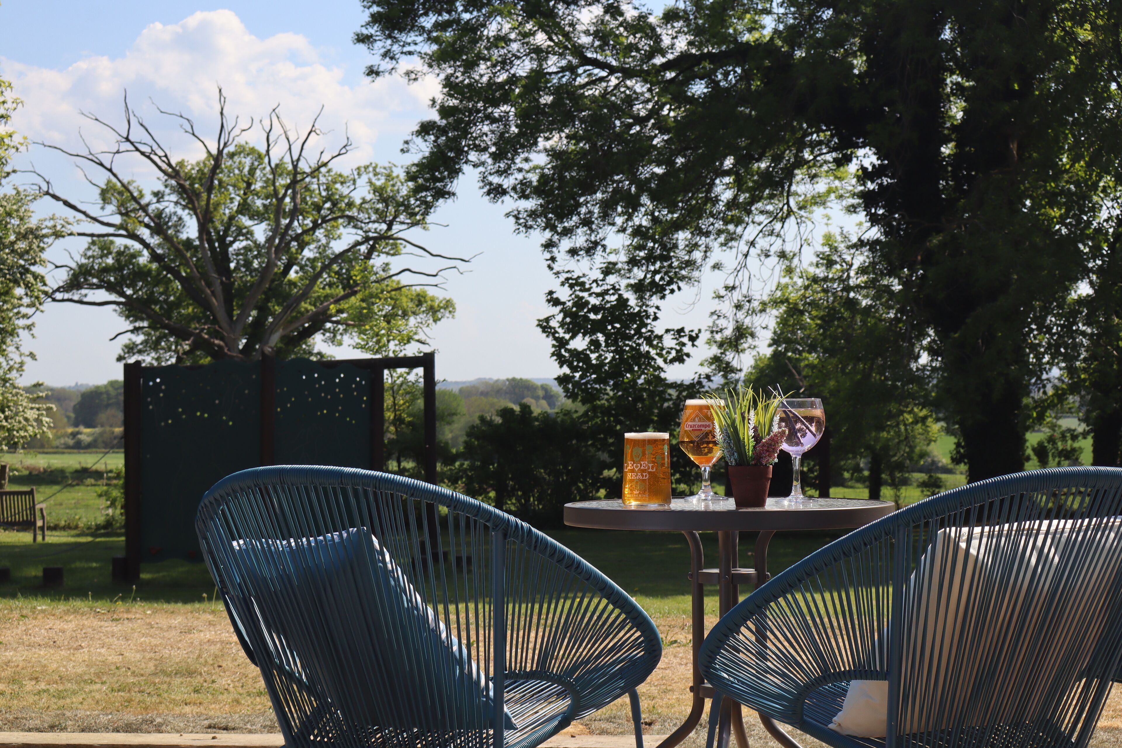 Un área de estar al aire libre con dos sillas azules y una mesa, una cerveza y una copa de vino.