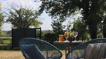 Un área de estar al aire libre con dos sillas azules y una mesa, una cerveza y una copa de vino.
