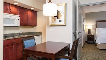A hotel room with a dining area featuring a wooden table and chairs, a microwave, a sink, and a framed artwork on the wall.