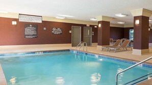 An indoor swimming pool with clear water, a lifeguard sign, and lounge chairs.