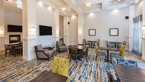 A hotel room with a large seating area, a flat-screen TV, and a patterned carpet.