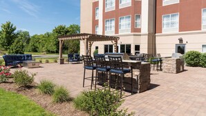An outdoor patio area with a barbecue station, seating, and a pergola.