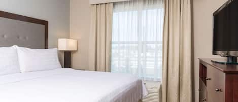 A hotel room with a large bed, a desk with drawers, a television, and a window with curtains.