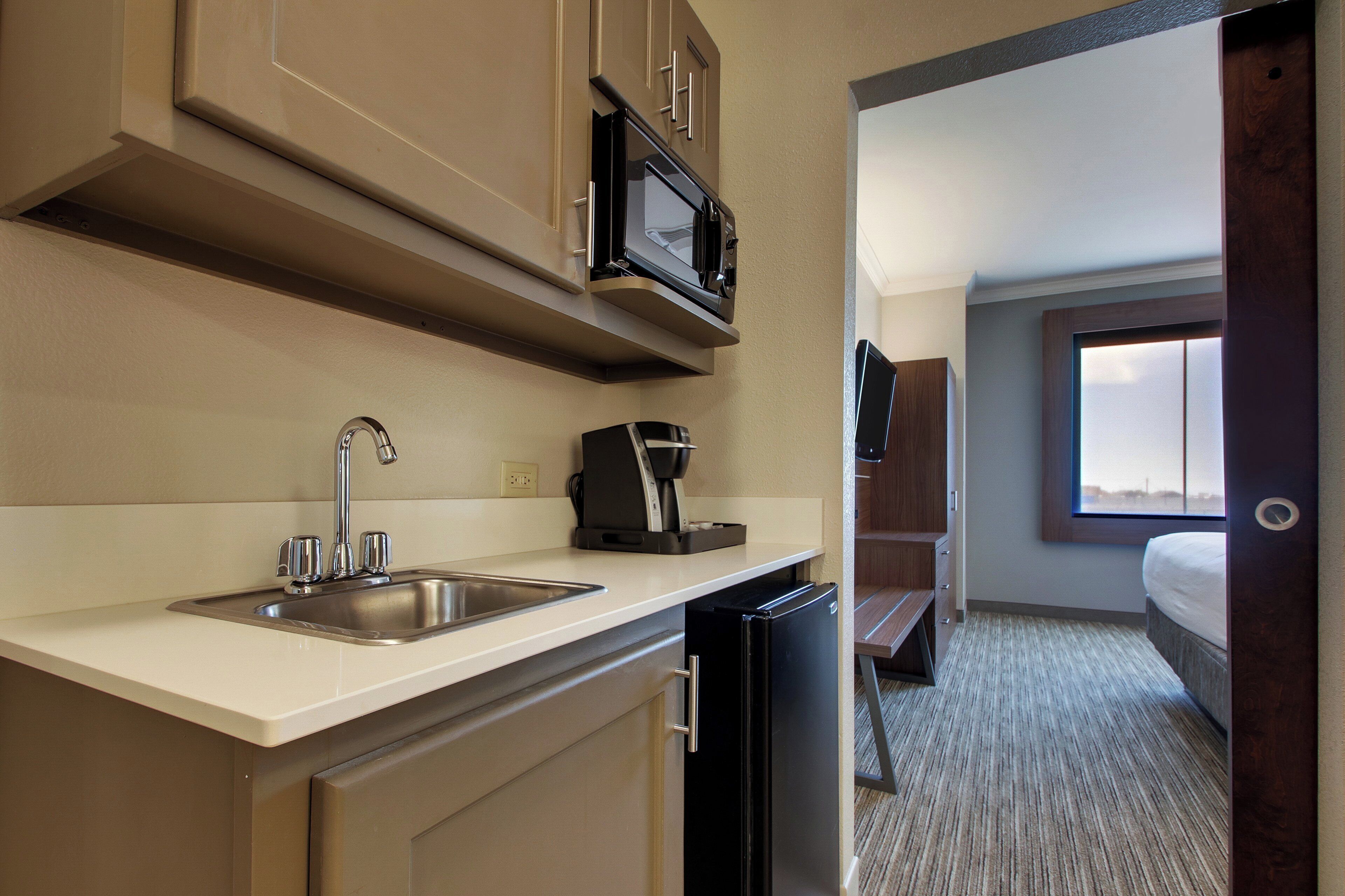 A compact hotel room with a kitchenette, including a sink, a coffee maker, and a refrigerator.