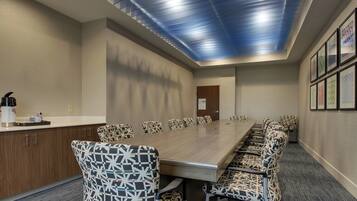 A conference room with a long table and patterned chairs, a wooden cabinet, and a door.