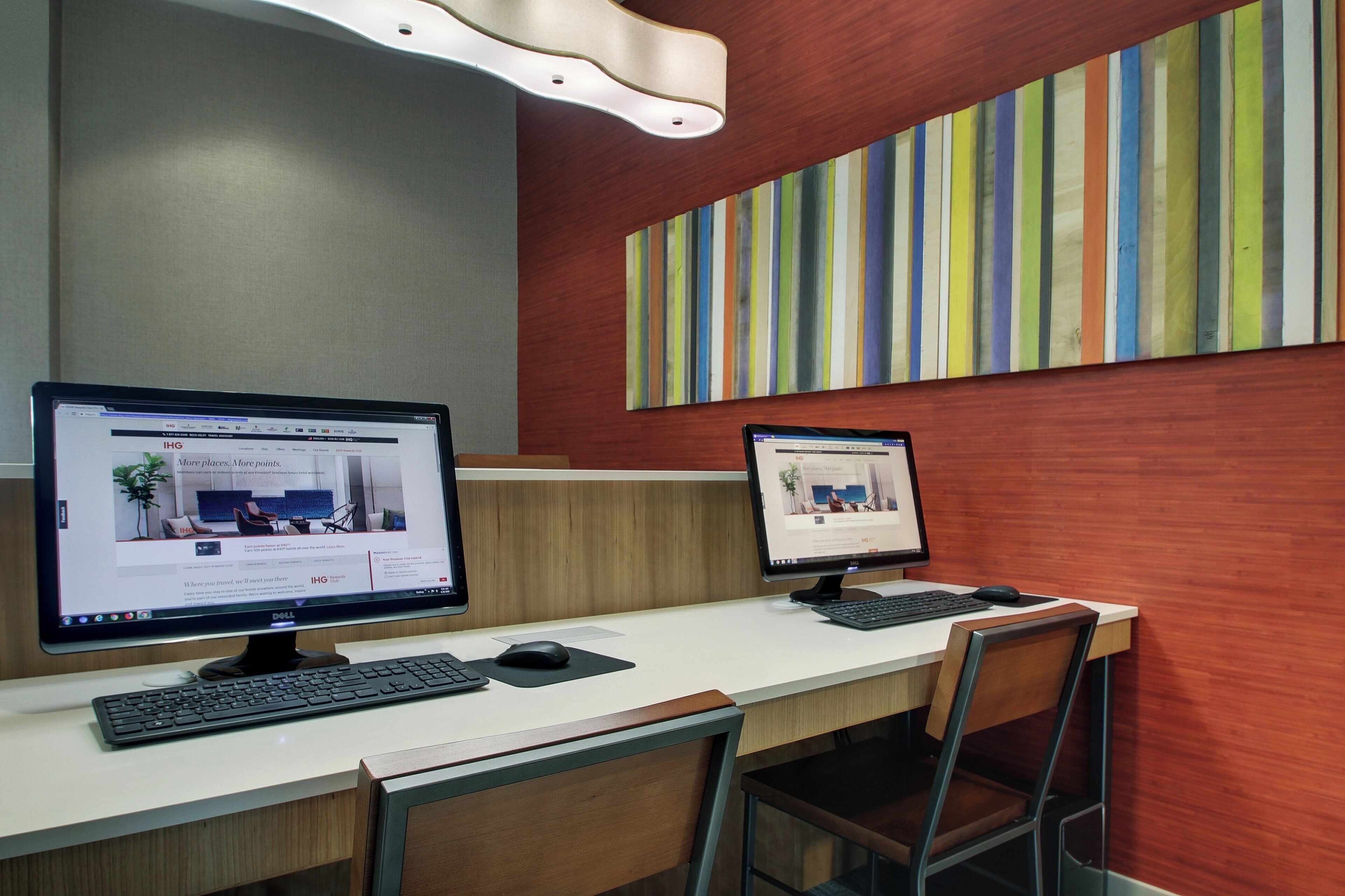Een moderne kantoorruimte met twee bureaureecomputers, een houten bureau en een kleurrijke gestreepte wand.