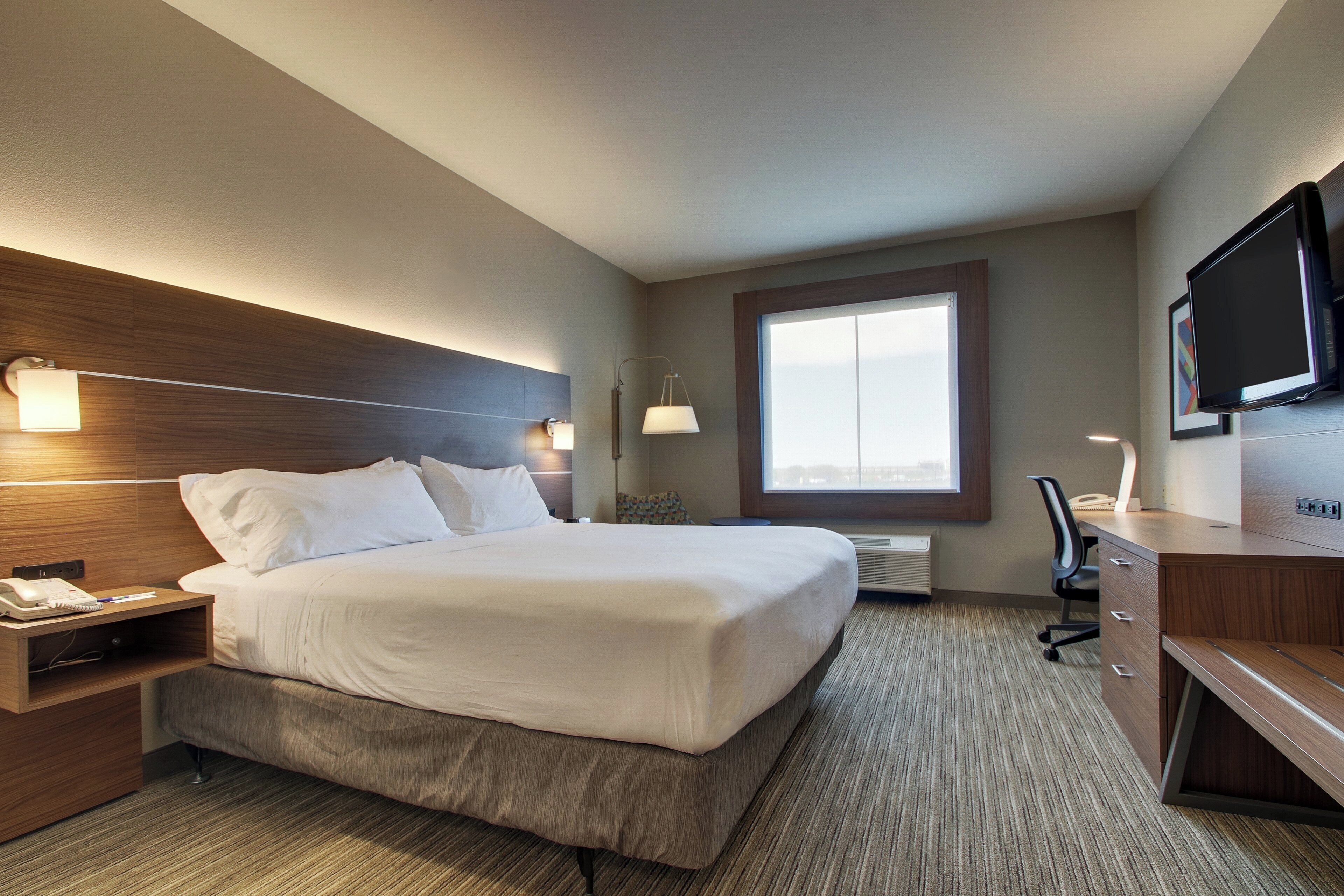 A hotel room with a large bed, bedside tables, a desk with a chair, a television, and a window.