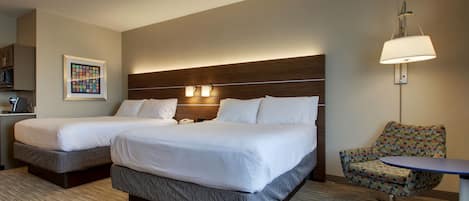 A hotel room with two beds, a small table, a chair, a lamp, and a framed picture on the wall.