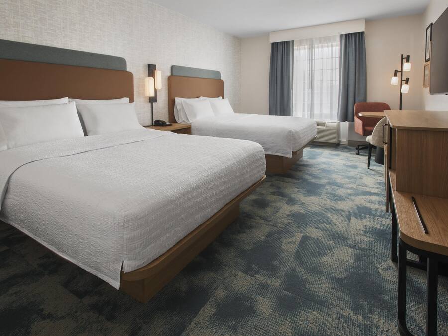 A hotel room with two beds, a desk, a chair, and a large window with curtains.