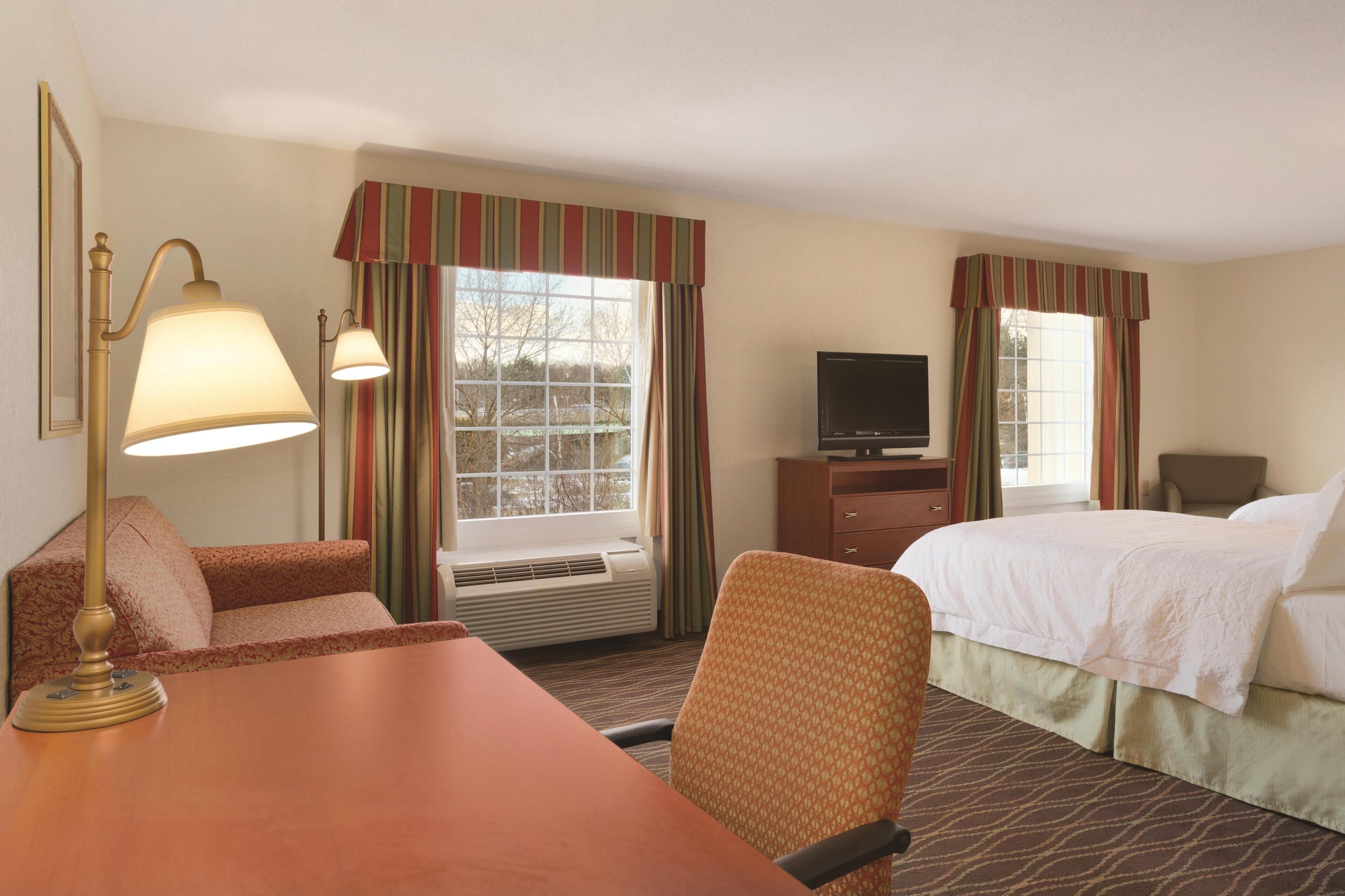 A hotel room with a bed, a desk, a chair, a television, and a window with curtains.