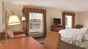 A hotel room with a bed, a desk, a chair, a television, and a window with curtains.