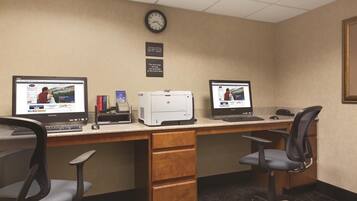 A hotel office with two computer desks, chairs, a printer, and a clock on the wall.