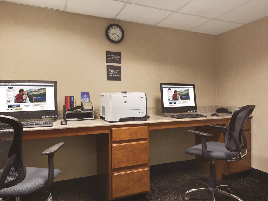 A hotel office with two computer desks, chairs, a printer, and a clock on the wall.