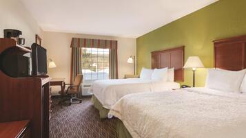 A hotel room with two beds, a desk with a chair, a television, and a window with curtains.