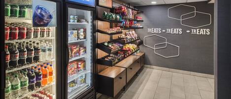 A beverage cooler with various drinks, a snack display, and a wall with 'TREATS' signage.