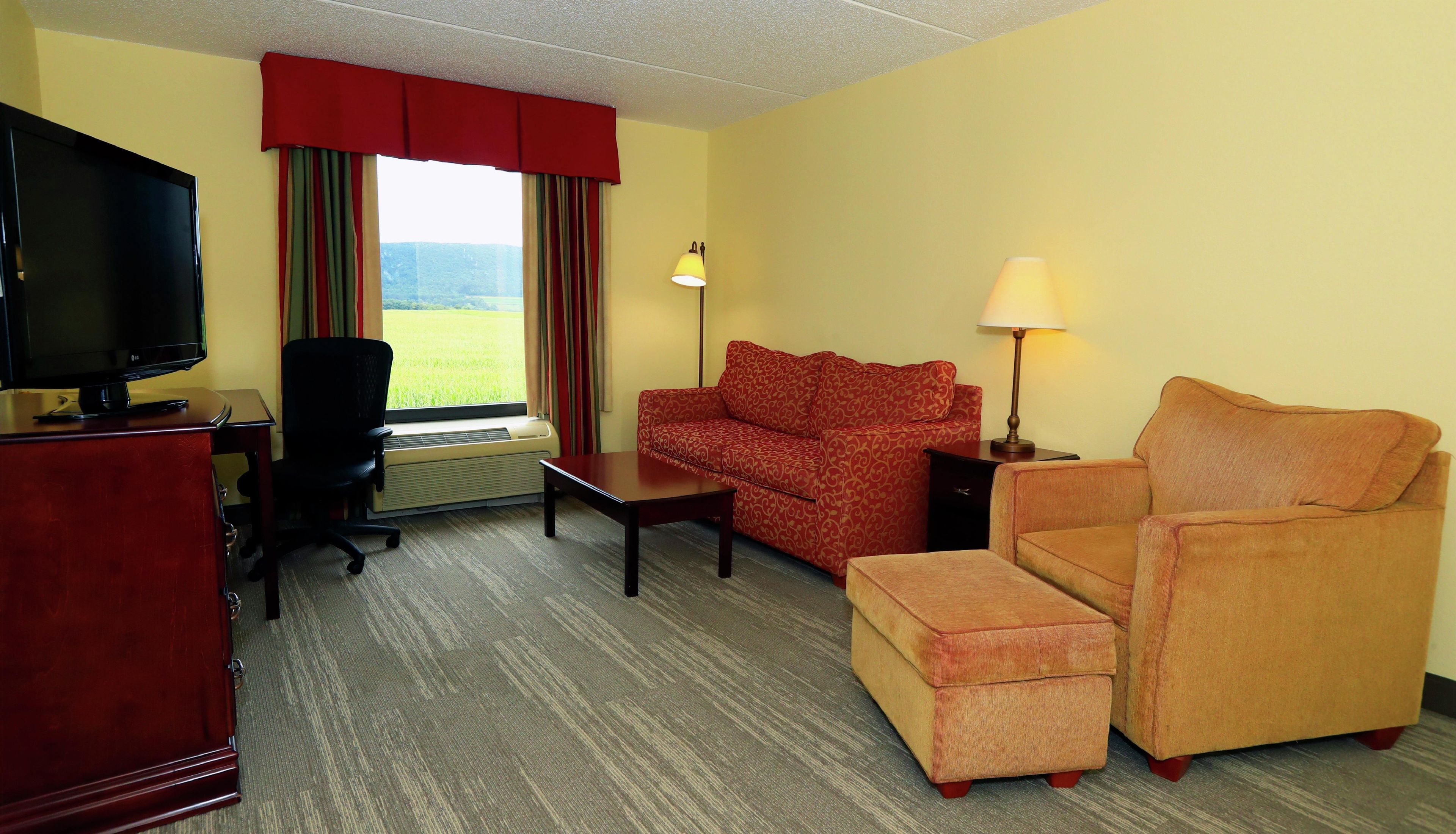 A hotel room with a TV, a sofa, a chair, a table, and a lamp.