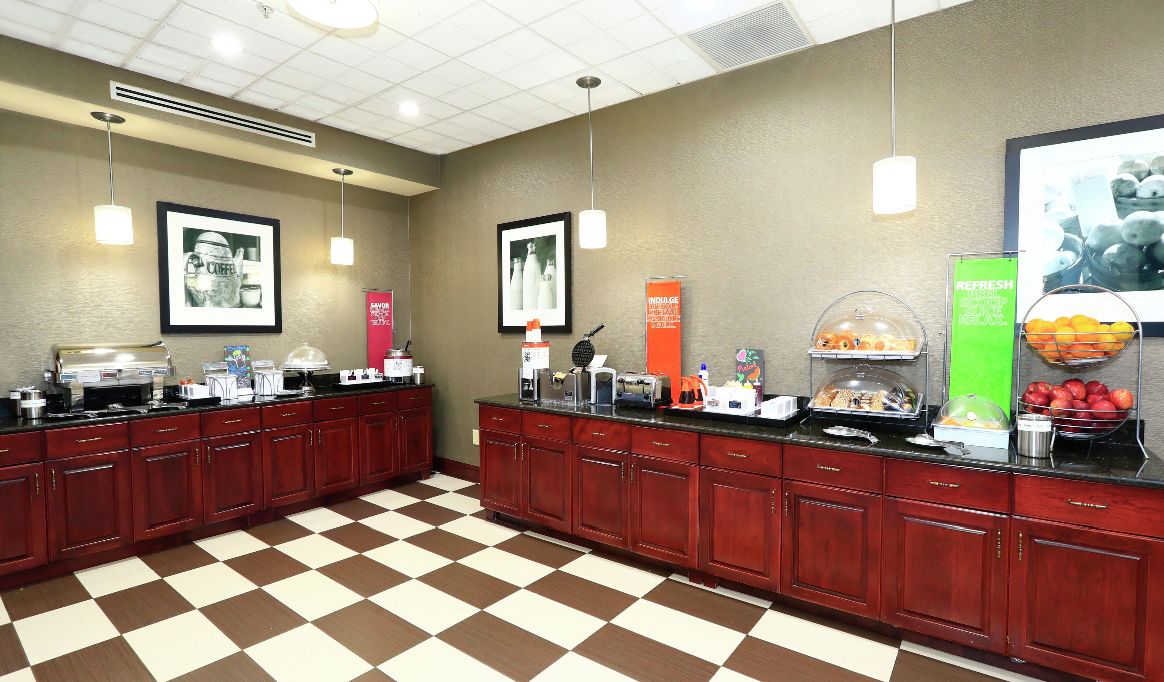 A hotel breakfast area with a checkered floor, a coffee station, and various food items displayed on the counter.