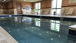 An indoor swimming pool with clear water, lounge chairs, and a tiled wall.