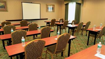 A conference room with multiple tables and chairs, a projector screen, and water bottles on the tables.