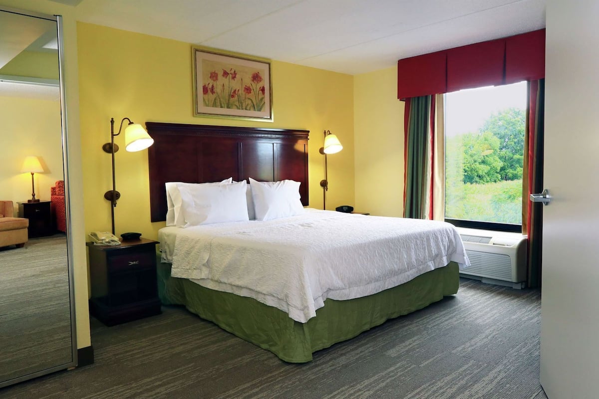 A hotel room with a bed, bedside lamps, a chair, a desk, a telephone, and a window with curtains.