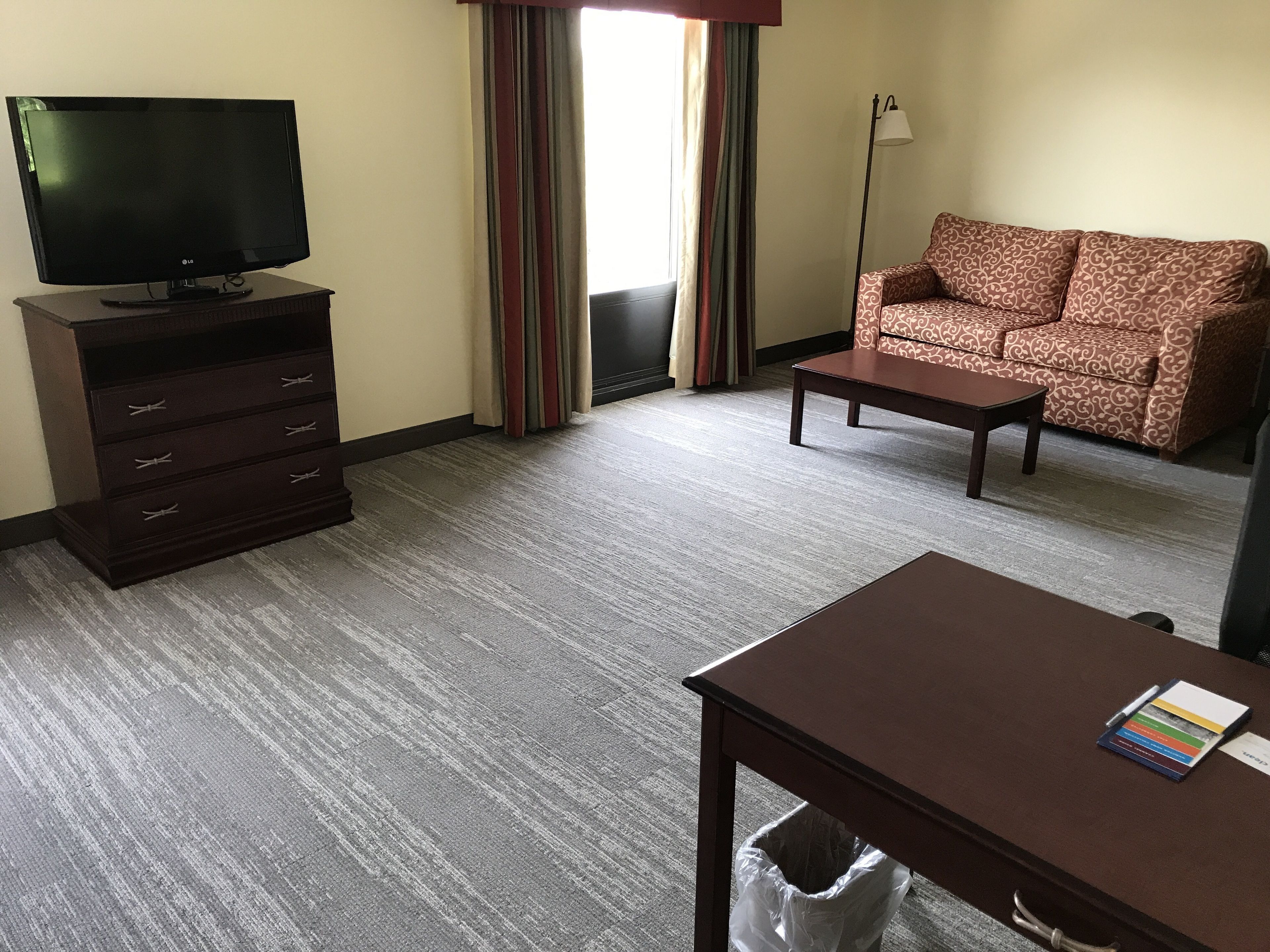 A hotel room with a flat-screen TV on a dresser, a sofa, a coffee table, and a trash can.