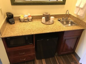 Cocina compacta con encimera de granito, cafetera, jarra de café, fregadero y lavavajillas.