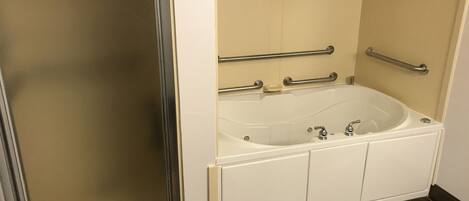 A bathroom with a glass shower enclosure, a white bathtub with grab bars, and a dark wood floor.