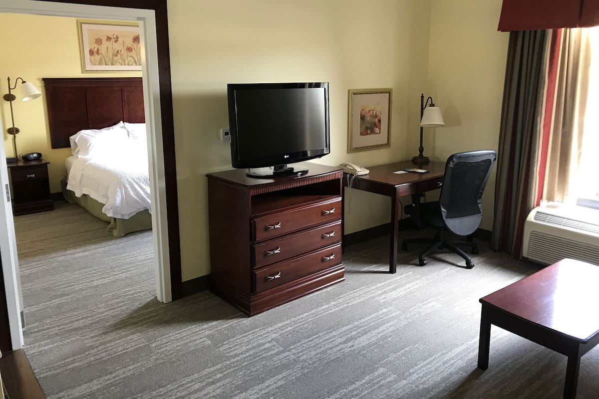 A hotel room with a bed, a desk, a television, a dresser, a chair, and a window with curtains.
