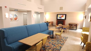 Un vestíbulo de hotel con un sofá azul, mesas de madera, sillas amarillas, un televisor y una chimenea.