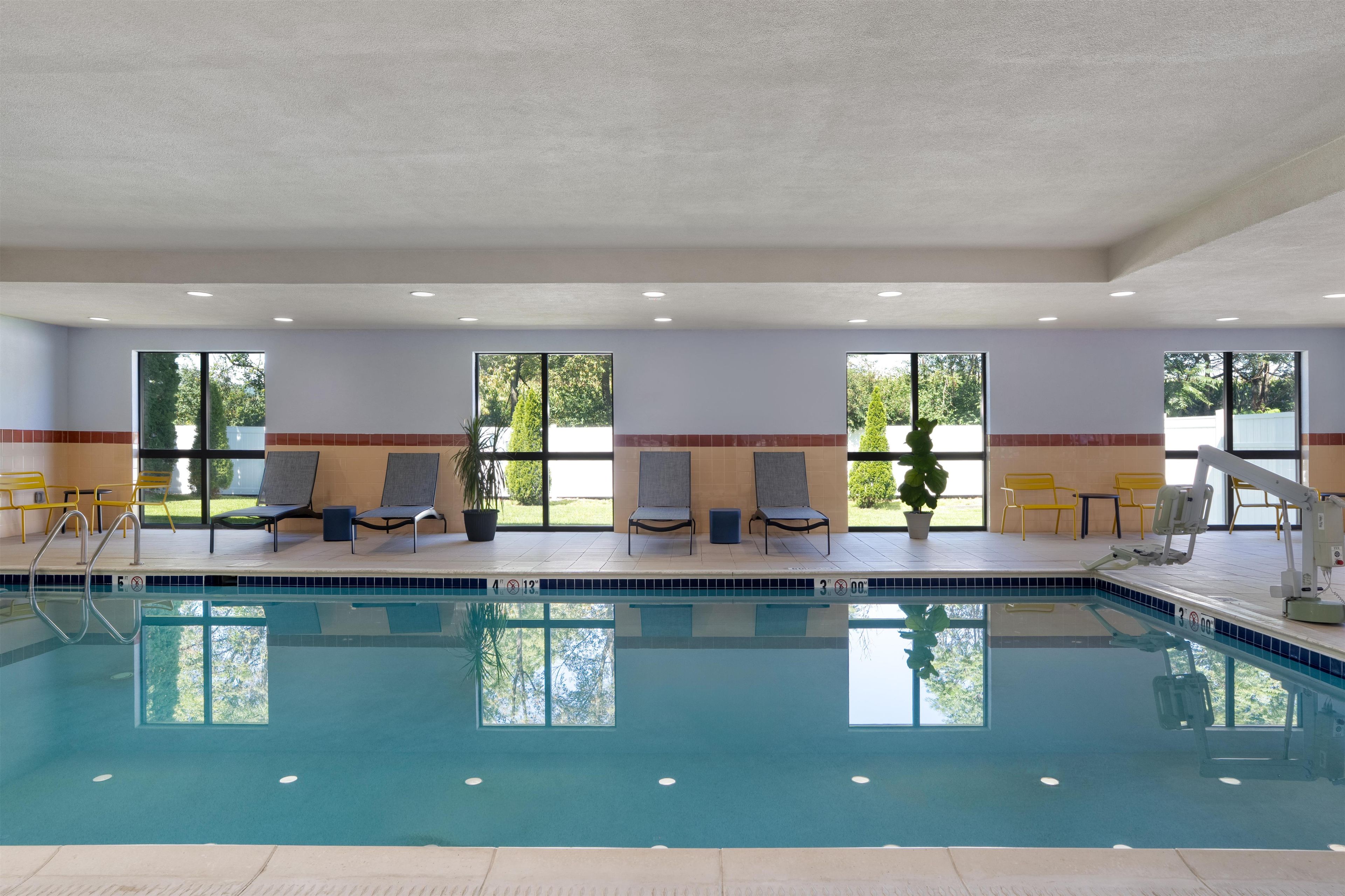 An indoor swimming pool with clear water, surrounded by lounge chairs and a view of greenery outside.