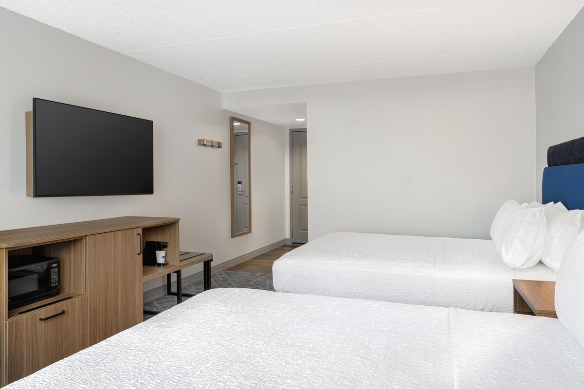 Habitación de hotel con dos camas, televisión, microondas y un escritorio pequeño.