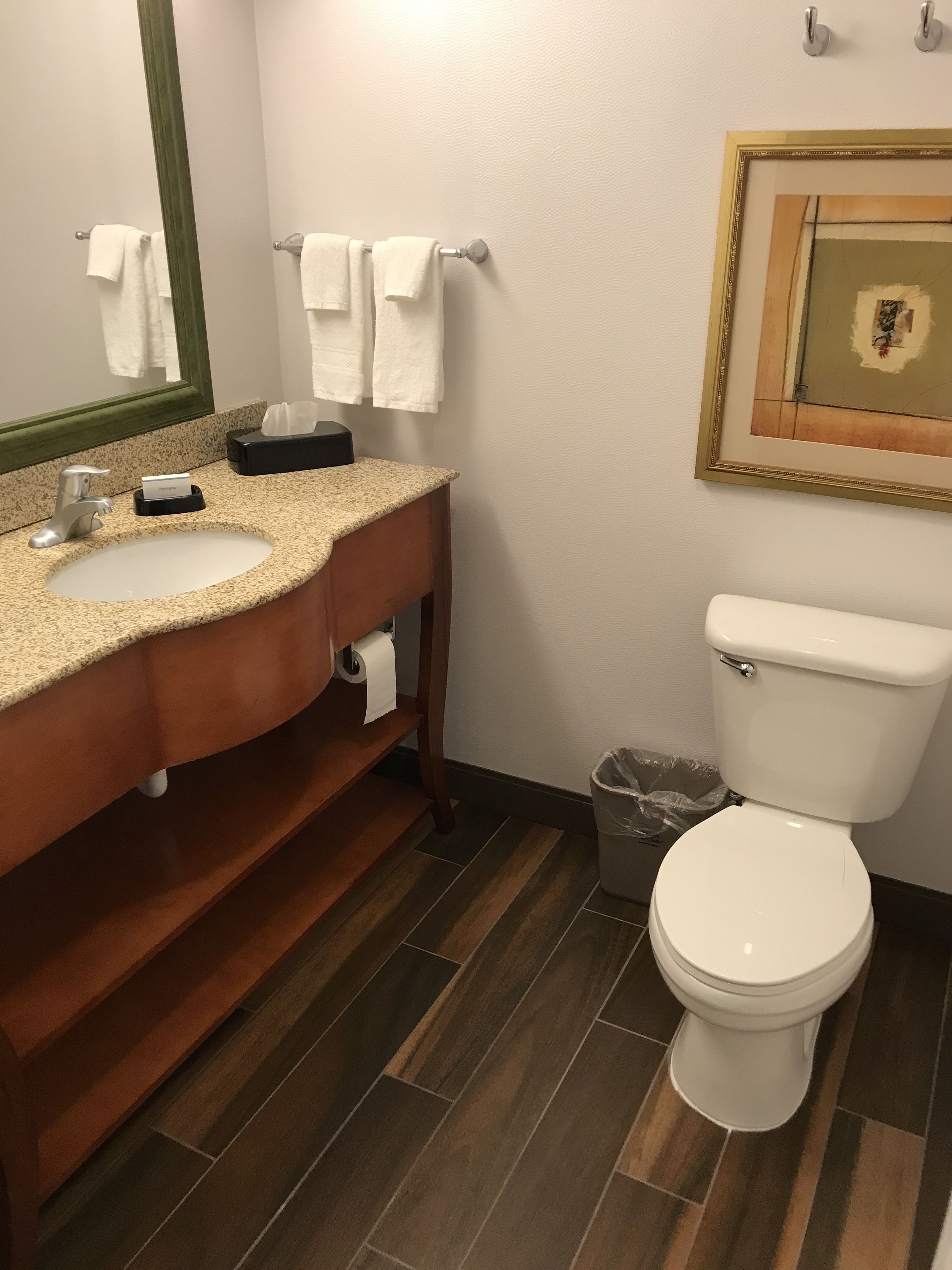 A bathroom with a wooden vanity, a sink, a toilet, and a trash can.