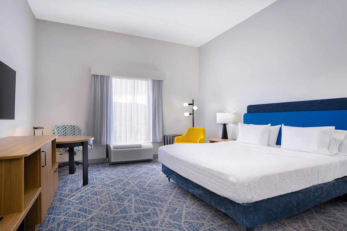A hotel room with a large bed, a desk, a chair, a lamp, and a window with curtains.