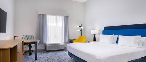 Una habitación de hotel con una cama grande, un escritorio, una silla, una lámpara y una ventana con cortinas.