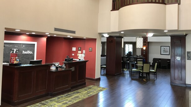 Zona de recepción de un hotel con mostrador de madera, pared roja y una escalera que sube a un nivel superior.