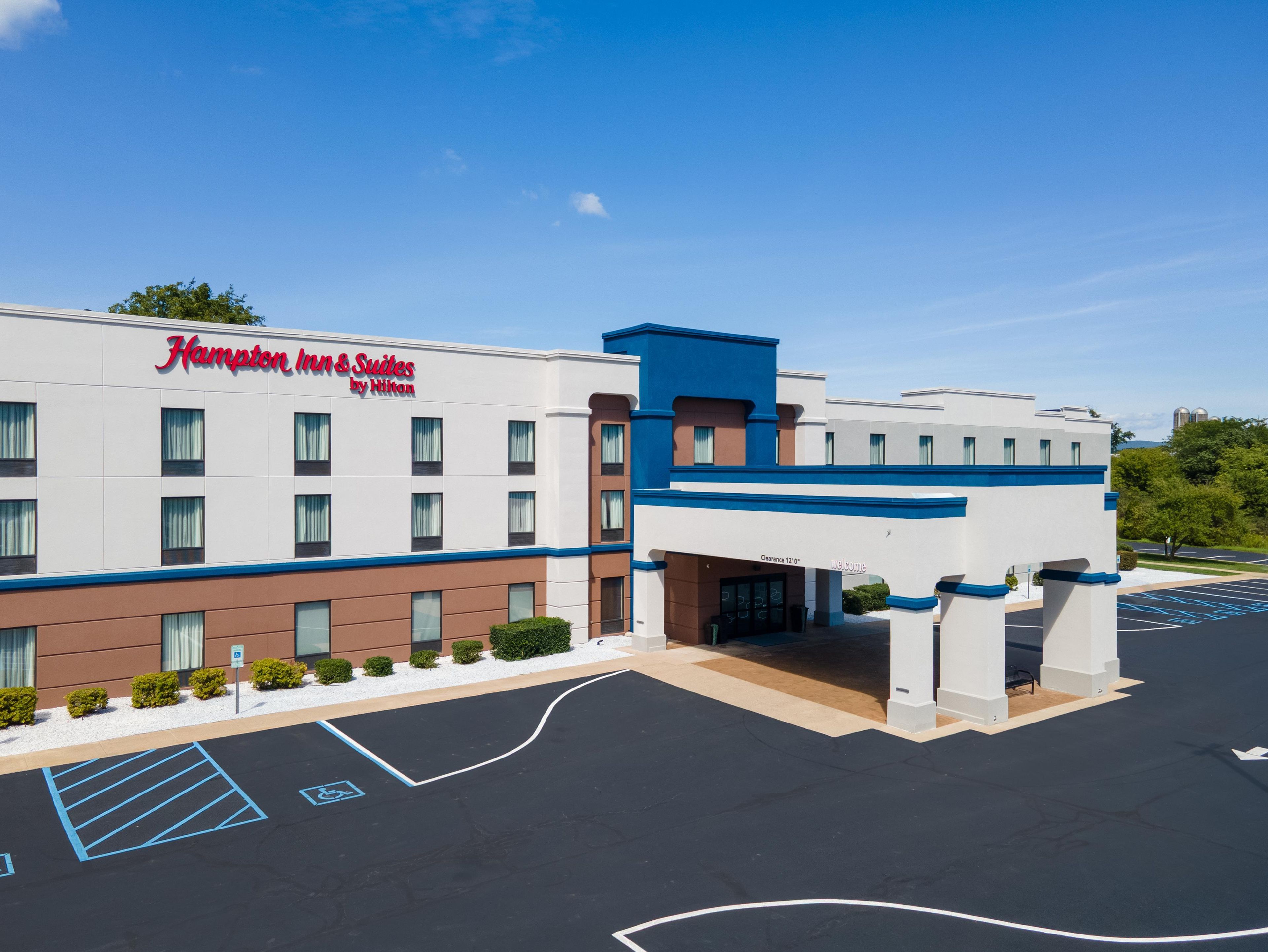 A Hampton Inn & Suites by Hilton with a clear sky, parking lot, and entrance.