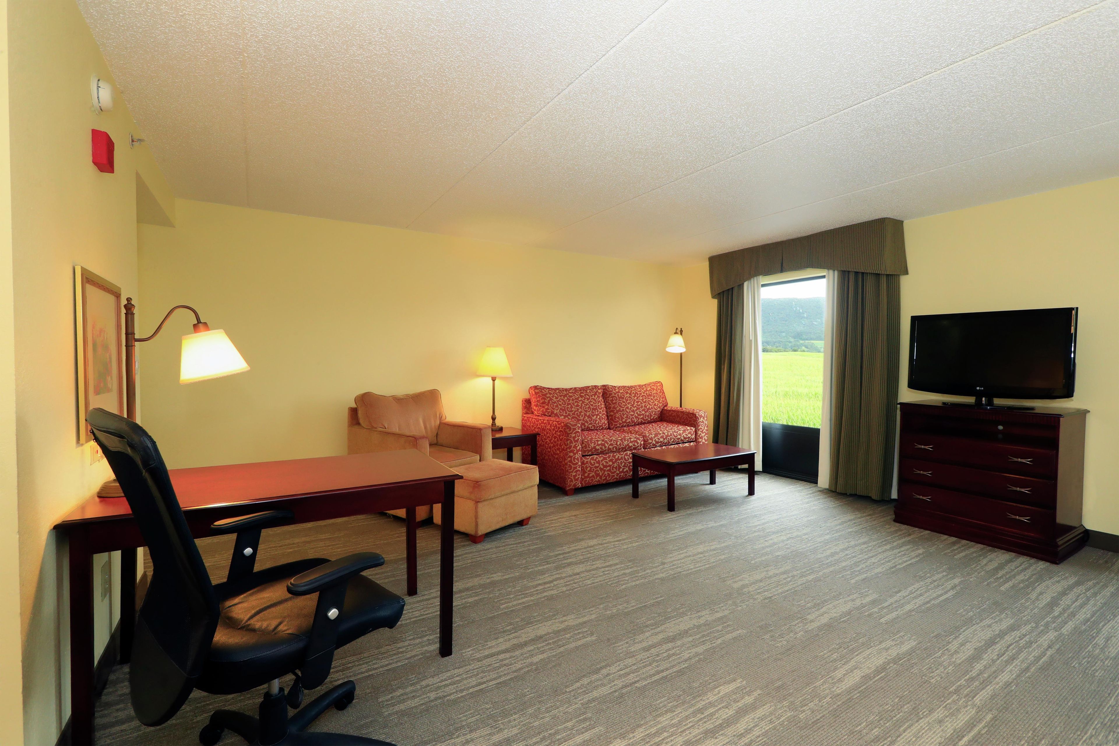 Een hotelkamer met een bureau, twee stoelen, een bank, een televisie en een raam met uitzicht.