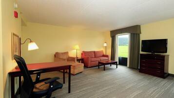 A hotel room with a desk, two chairs, a sofa, a television, and a window with a view.