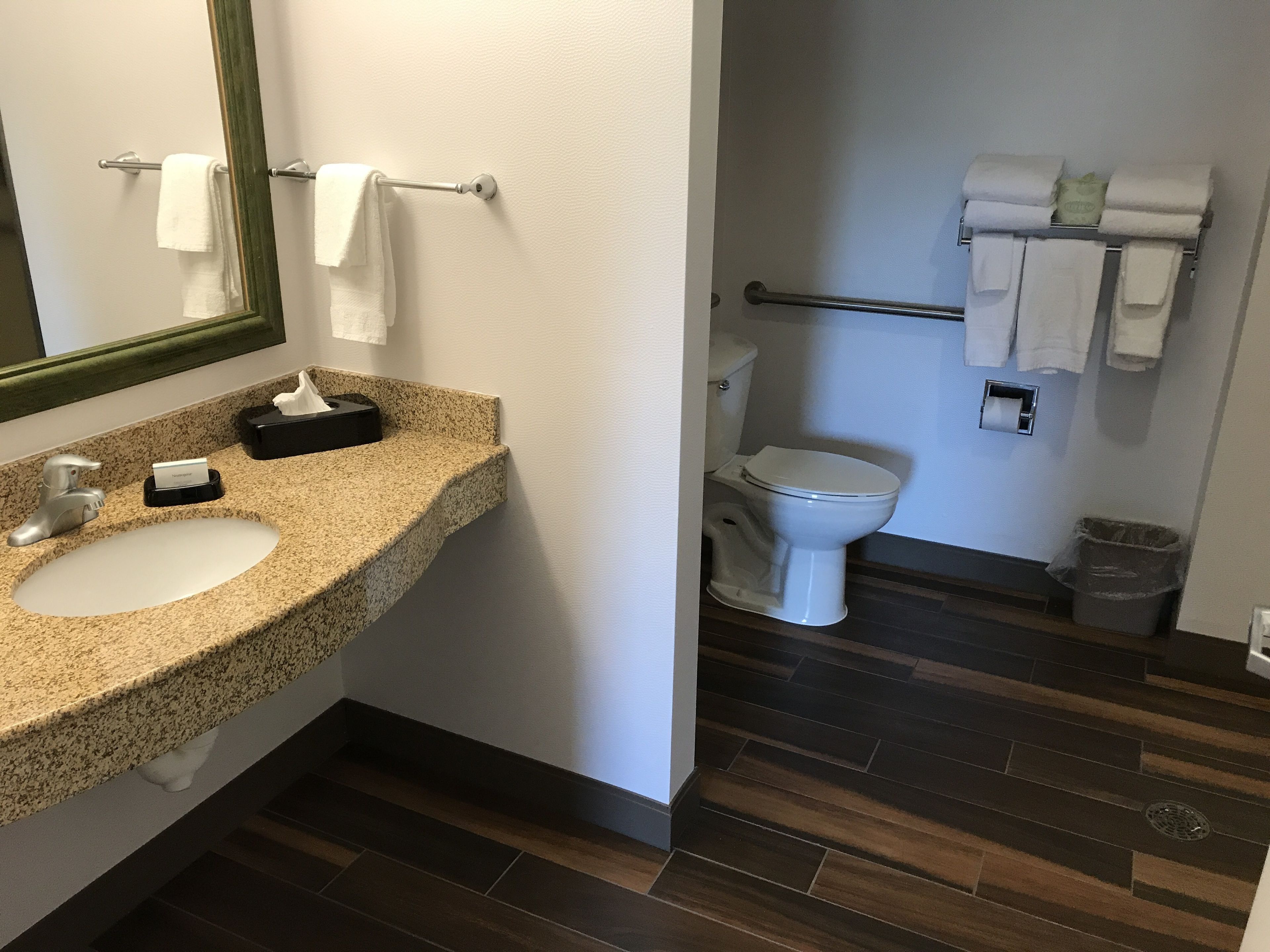 A bathroom with a granite countertop sink, a mirror, a toilet, and a towel rack.