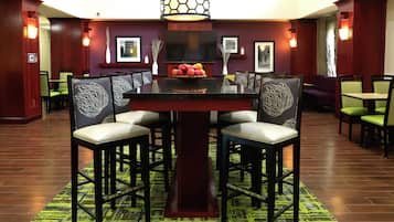 Un comedor de hotel con una mesa central rodeada de sillas, un televisor sobre la mesa y cuadros en las paredes.