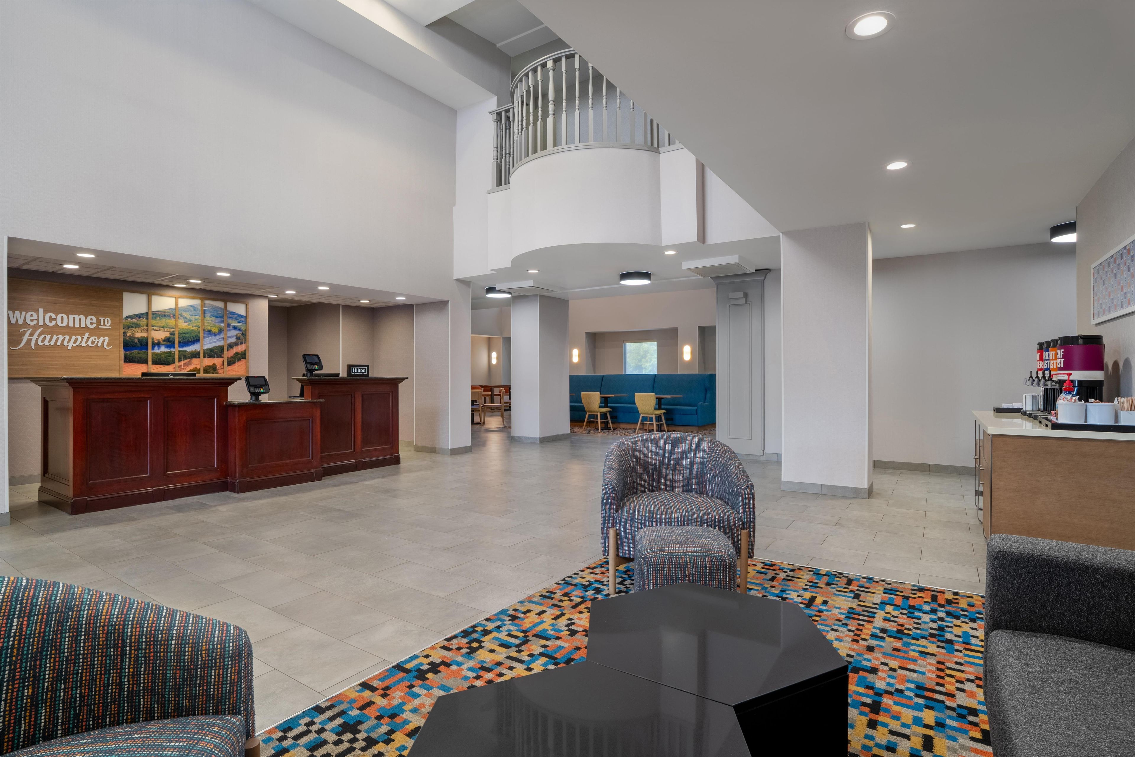 A hotel lobby with a reception desk, seating area, and a staircase leading to an upper level.