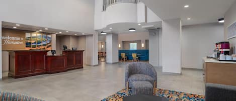 A hotel lobby with a reception desk, seating area, and a staircase leading to an upper level.