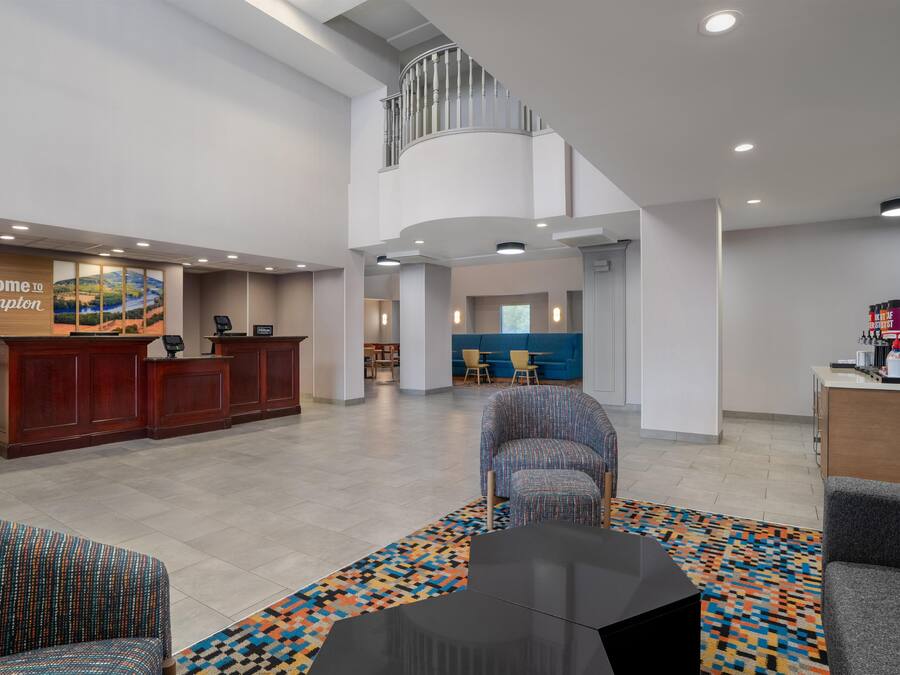 A hotel lobby with a reception desk, seating area, and a staircase leading to an upper level.