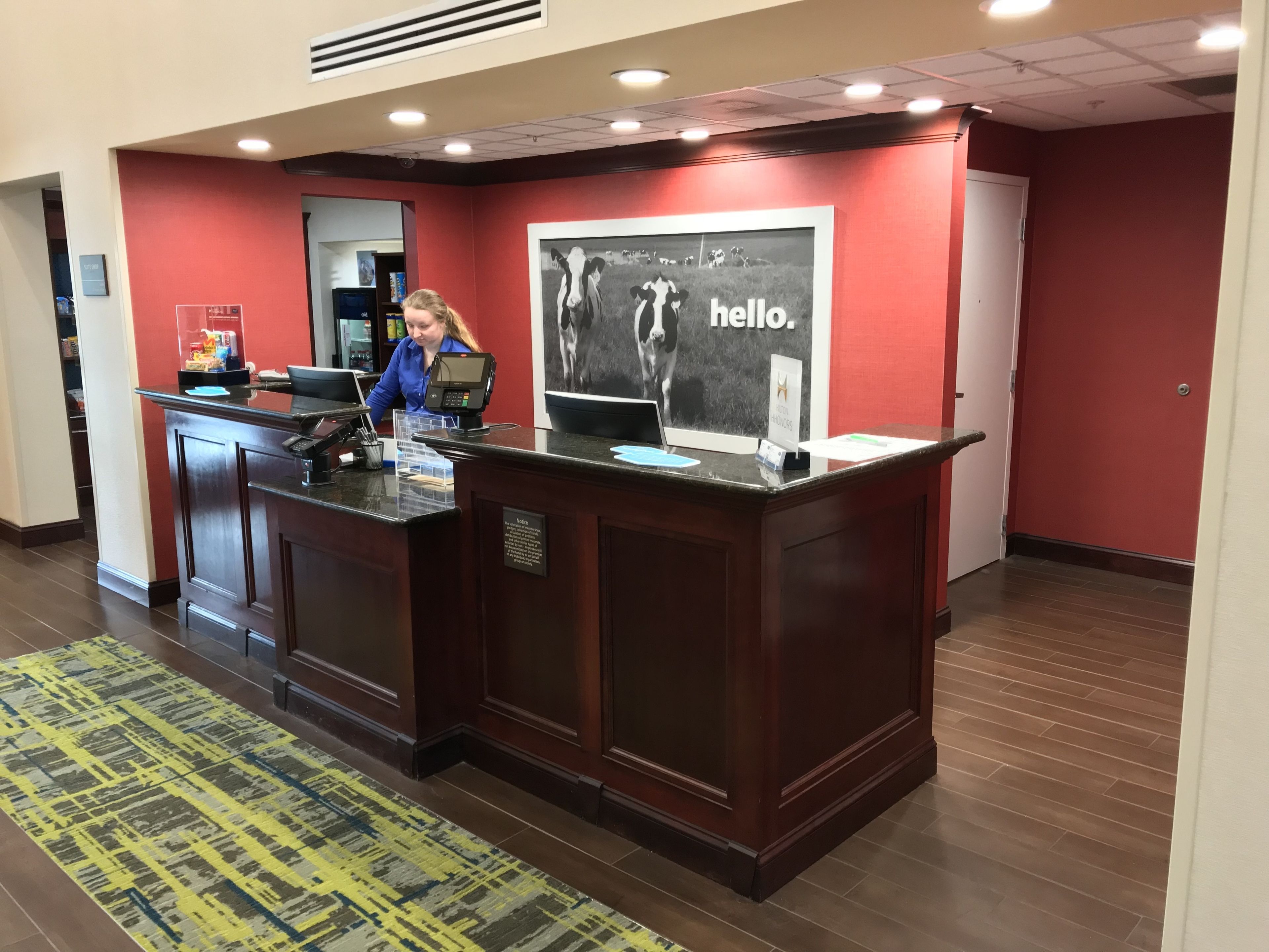 Un mostrador de recepción con un quiosco digital, un cartel que dice 'hello' y una alfombra estampada.
