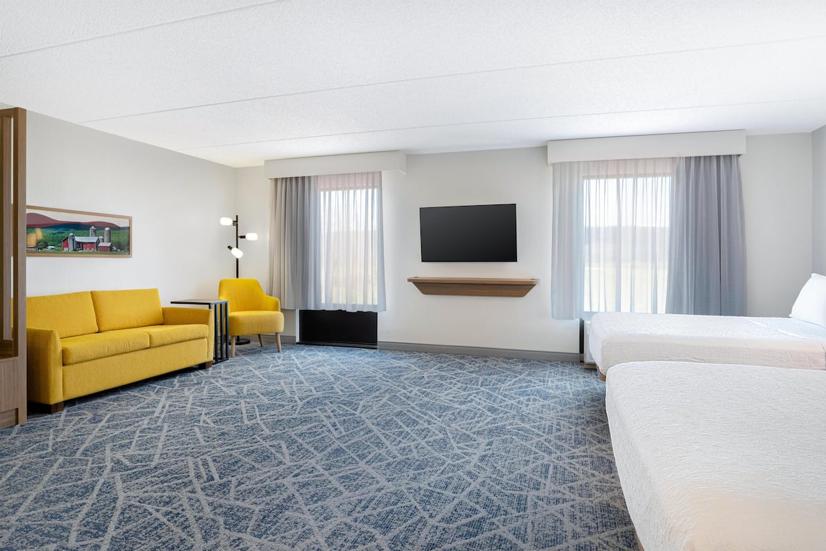 A hotel room with a sofa, a chair, a bed, a TV, and a painting on the wall.