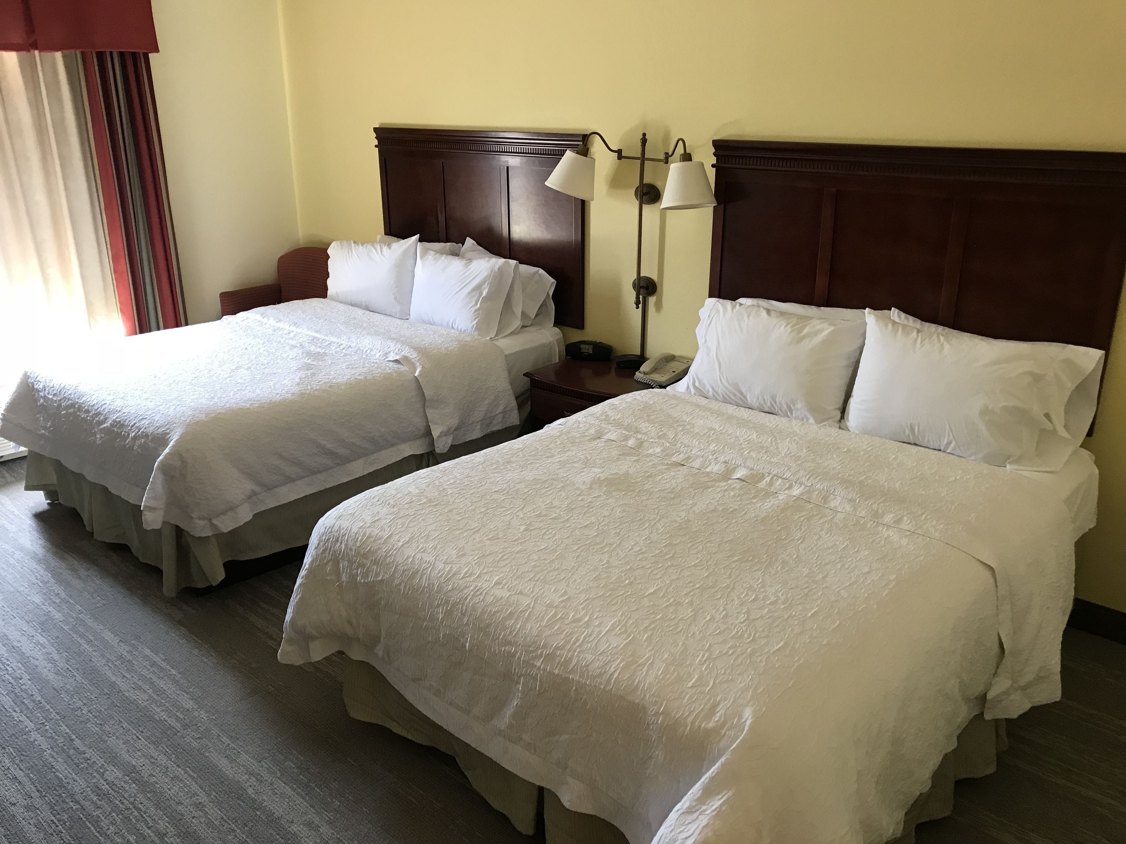 A hotel room with two single beds, a wooden headboard, a bedside table with a lamp, and a telephone.