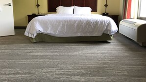 A hotel room with a large bed, two bedside lamps, a nightstand, a window with curtains, and an air conditioning unit.