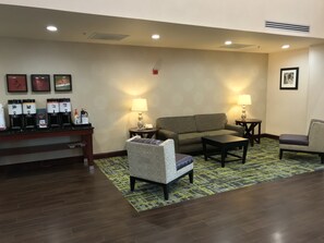 A lobby with a reception desk, coffee machines, a sofa, two armchairs, and a patterned rug. - Hampton Inn & Suites Lamar (Mill Hall)
