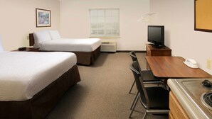 Ein Hotelzimmer mit zwei Betten, einem Fernseher, einem Schreibtisch mit Telefon und einem Fenster mit Jalousien.