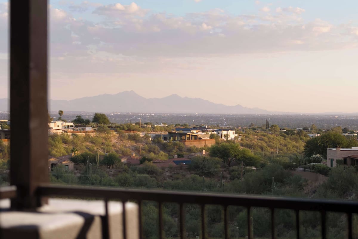 Une vue depuis un balcon donnant sur un quartier résidentiel, avec des maisons, des arbres et des montagnes au loin.